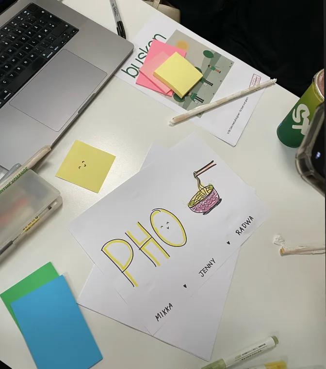 Arbeidsbordet på UX Cup-dagen, med PHO-skiltet, post-it-lapper og busken-caset